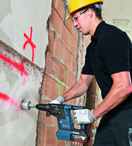 Ein Mann bohrt mit dem Bosch Akku-Bohrhammer GBH 18V-26F ein Loch in eine Wand